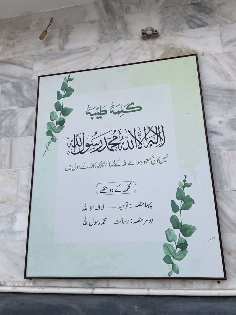 کلمہ طیبہ کا بورڈ جس کے کنارے پر سبز پتوں کی بیل بنی ہے۔