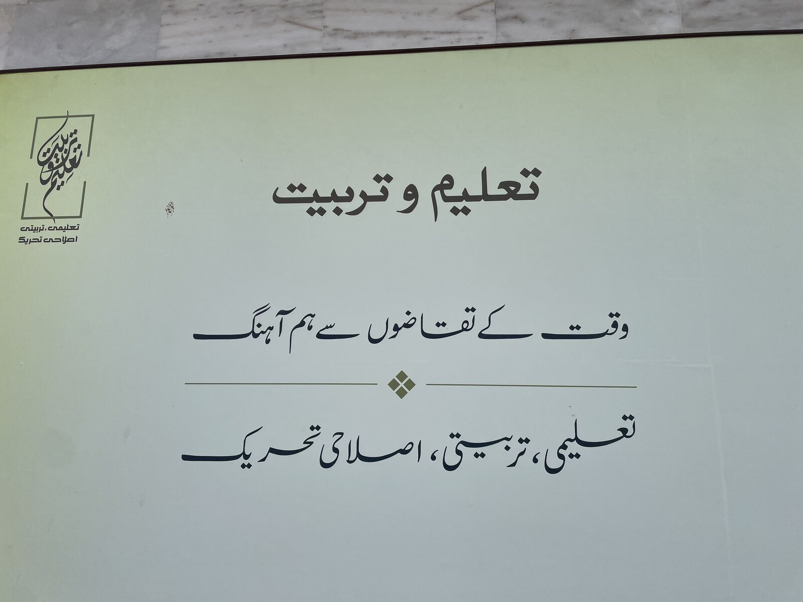 ہلکے سبز رنگ کا بورڈ جس پر نستعلیق میں «تعلیم و تربیت» لکھا ہے۔